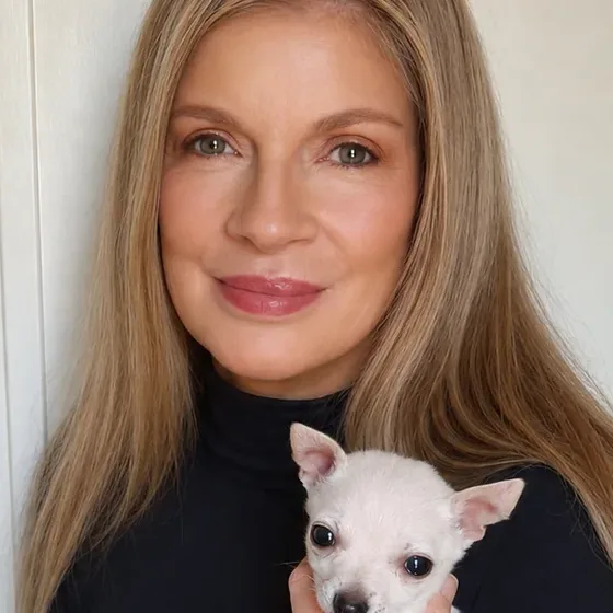 Jill in a black turtleneck, holding a small white chihuahua puppy against her chest